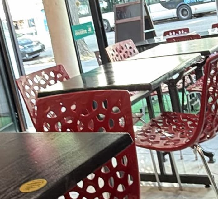 Tables et chaises rouges ajourées de la salle, devant les baies vitrées donnant sur l’avenue